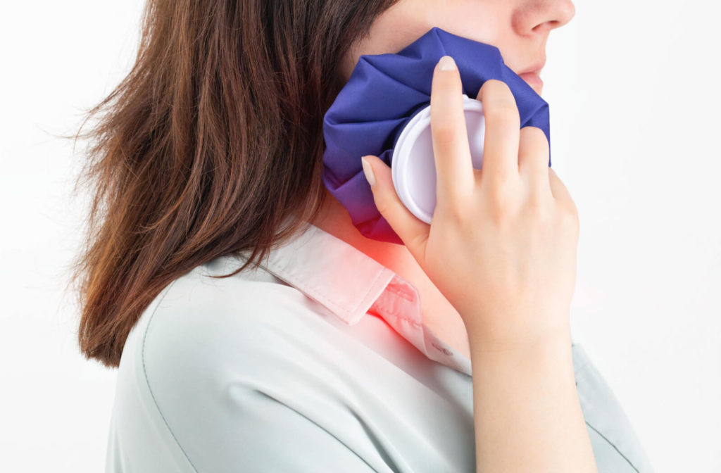 A woman facing sideways and holding a blue hot compress bag placed on her right jaw to alleviate the symptoms of tmj