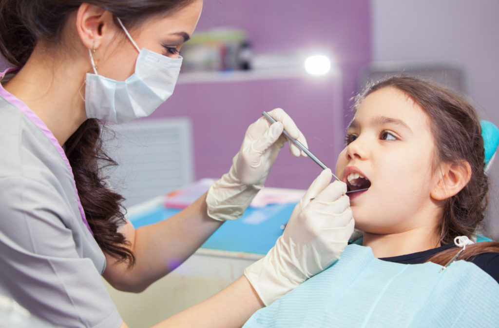 A female dentist is holding a dental mirror and examining a crack tooth of a female child.