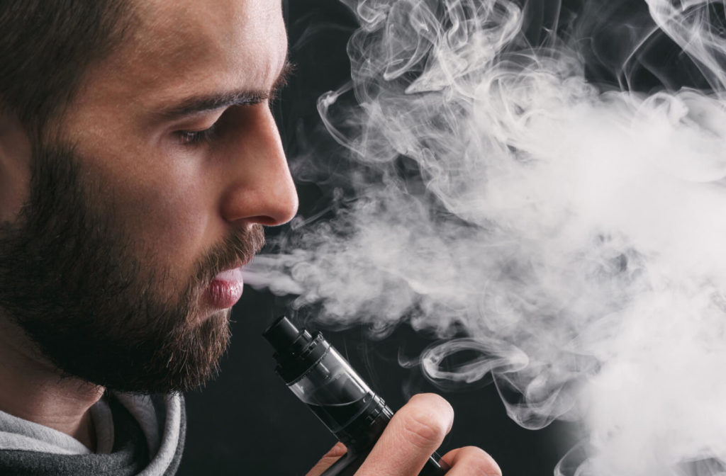 A man holding an electronic cigarette and exhaling a large cloud of vapour.