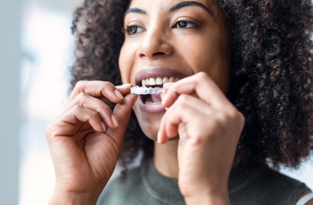 A close-up of a woman putting on an Invisalign brace.