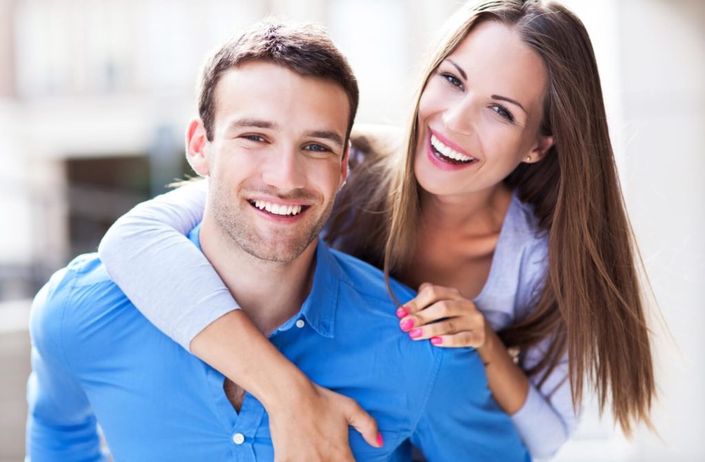 A young couple smiling, both showing their beautiful and healthy looking teeth.