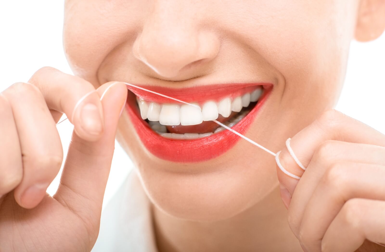 A close-up image of a woman smiling while flossing her teeth.