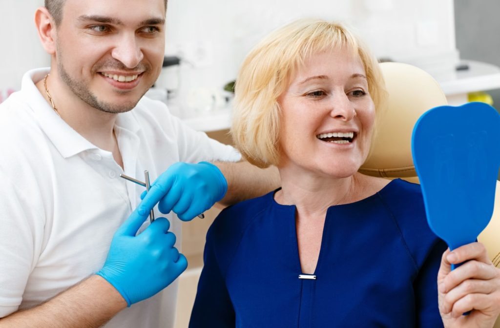 A dentist and a patient smiling while they look in a small handheld mirror admiring the new all-on-4 dental implant.