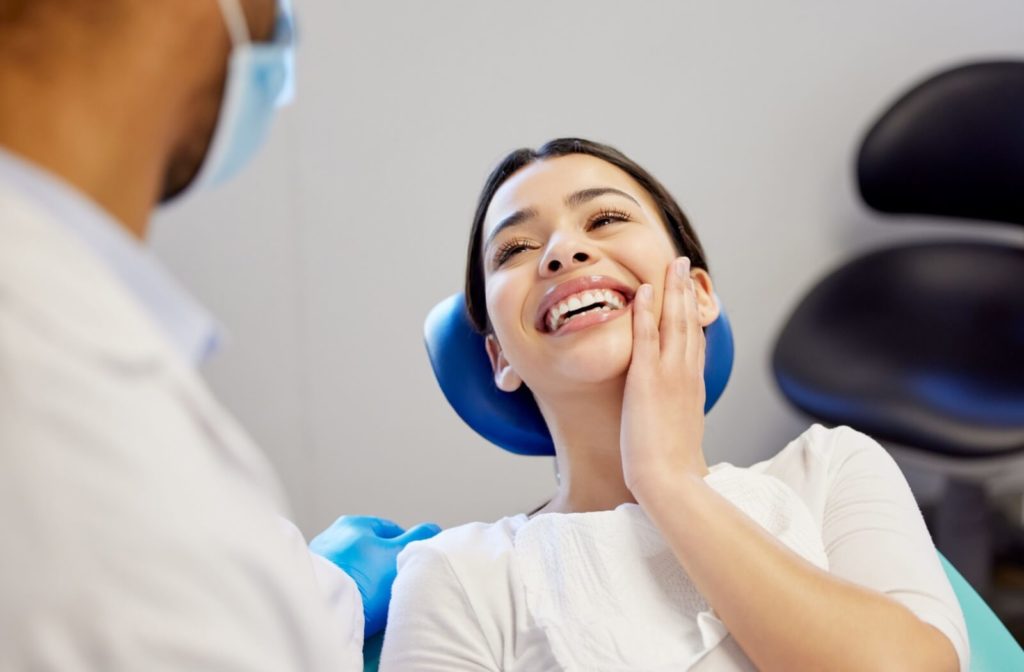 A smiling dental patient grins up at their dentist while holding a hand to their restored smile