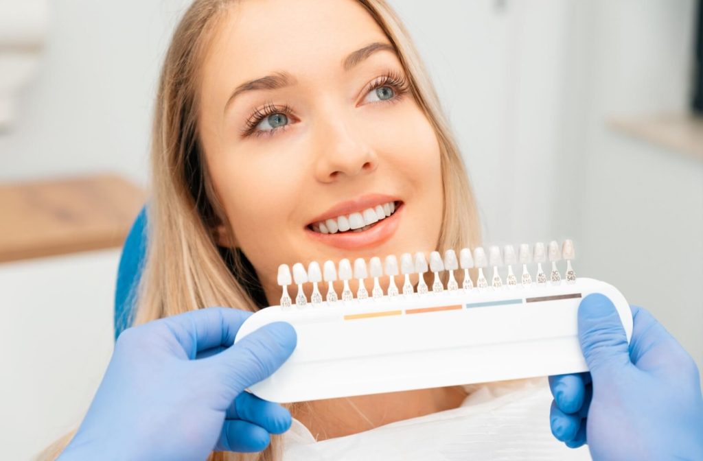 An optometrist holds up several shades of dental veneers to a patient’s mouth to pick a matching shade