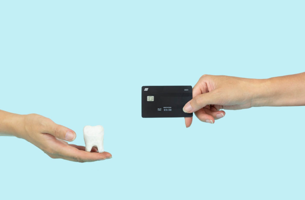 Against a blue background, a hand on the left holds out a giant tooth while a hand on the right holds out a credit card